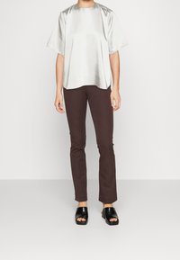 Haut argenté à manches courtes avec un col rond, associé à un pantalon moulant marron foncé. Sandales plates noires à bout ouvert avec des accents texturés.