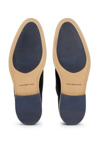 Semelles de chaussures en cuir suédé noir avec des bords en cuir tan, présentant une finition lisse et un embossage de logo. Grip en caoutchouc texturé pour la traction.