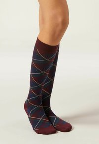Calcetines hasta la rodilla en burdeos con un patrón de diamantes en azul marino, verde y blanco. Textura suave y puños de color sólido en la parte superior.