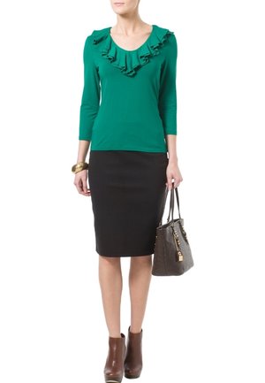Haut vert avec un col froncé, manches trois-quarts, associé à une jupe noire ajustée. Bottines marron et un sac à main en cuir texturé marron.