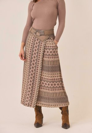 Mujer que lleva una falda envolvente con estampado geométrico, una camiseta de manga larga acanalada, un cinturón ancho y botines de ante marrones.