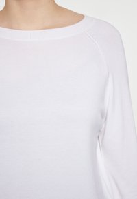 Weißer Strickpullover mit weitem Ausschnitt und langen Ärmeln, aus weichem Material und mit dezenten Nähten entlang der Säume.