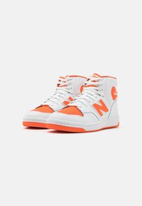 Vysoké tenisky vyrobené z bílé kůže s oranžovými akcenty, s perforovanou špičkou, polstrovaným límcem a jazykem, a texturovanou gumovou podrážkou.