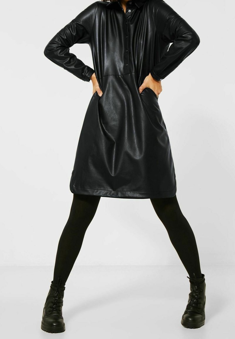 Svart kjol i konstläder med knäppning framtill, långa ärmar och sidofickor. Har en lös passform och en mjuk textur.