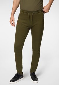 Oliwkowe dresy wykonane z miękkiego materiału, z paskiem ze sznurkiem, bocznymi kieszeniami na zamek oraz tonowymi akcentami tekstowymi wzdłuż nogawek.