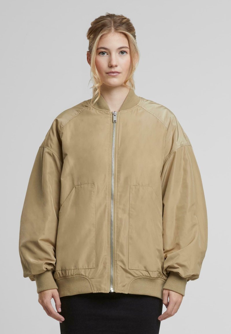 Khaki värvi bomber-jakk, mis on valmistatud siledast kangast, millel on ees lukuga sulgur, kaks külge taskut, ribakudumine mansettides ja lõdvestatud istuvus.