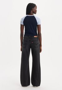 T-shirt à manches courtes bleu marine et bleu clair avec un pantalon en jean noir taille haute et large. Étiquette rouge Levi's visible sur la poche arrière.