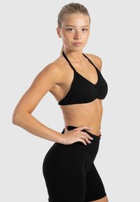 Zwarte haltercrop top met geplooid detail en hoge zwarte shorts. Soepele, rekbare stof tegen een lichtgrijze achtergrond.