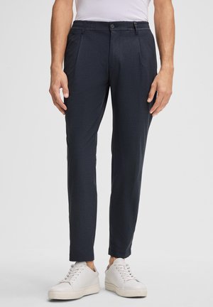 Pantaloni navy realizzati in tessuto testurizzato con vestibilità slim, dotati di chiusura con bottone, vita elastica e tasche anteriori. Abbinati a scarpe bianche.