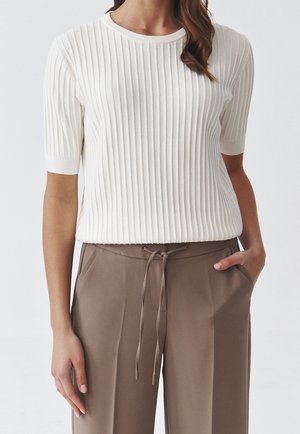 Weißer, kurzärmliger, gerippter Pullover mit rundem Ausschnitt, kombiniert mit braunen, locker sitzenden Hosen mit Kordelzug in der Taille und Taschen.