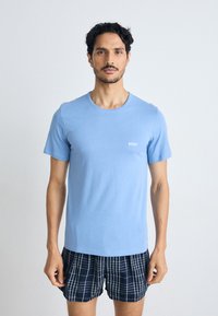 T-shirt de manga curta azul claro com decote redondo, apresentando um pequeno logótipo branco "BOSS". Combinado com calções aos quadrados em azul-marinho.
