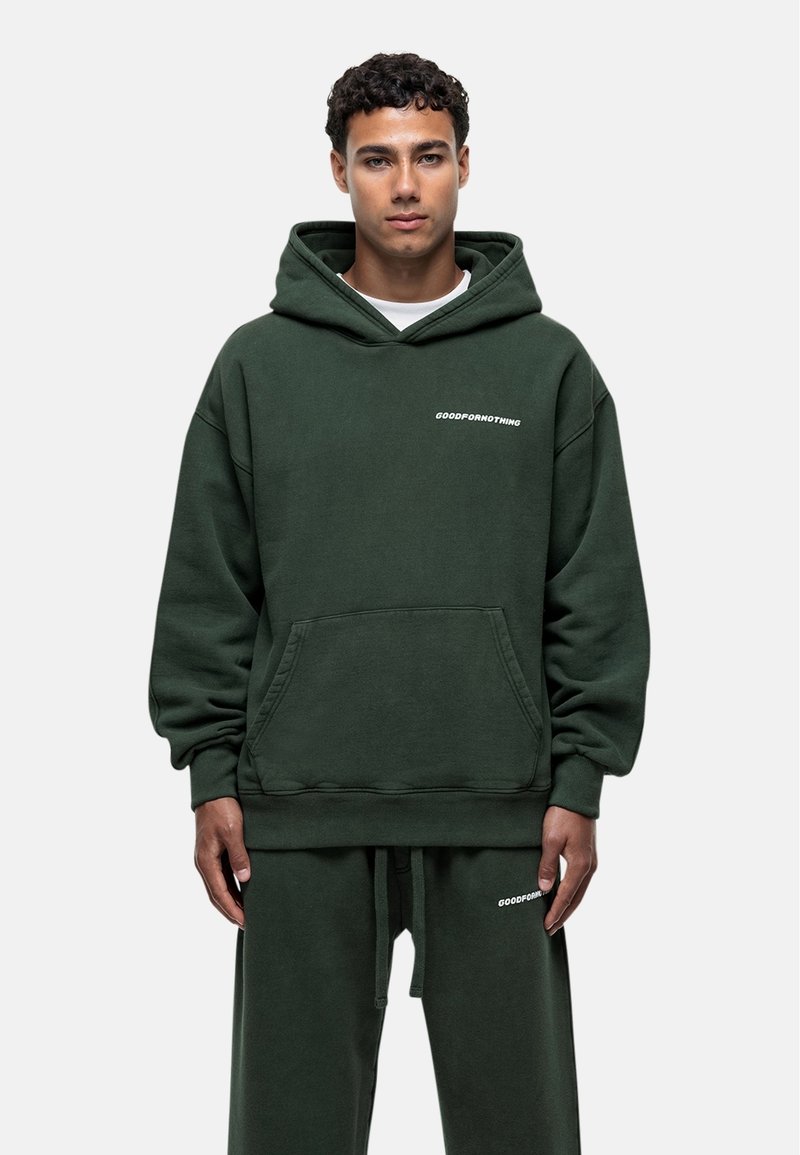 Ciemnozielona bluza z kapturem z kieszenią z przodu, z białym napisem "GOODFORNOTHING", luźny krój, miękka struktura, w zestawie ze spodniami dresowymi w tym samym kolorze.