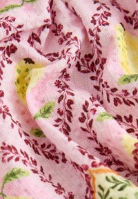 Tissu tricoté rose avec des motifs floraux rouges en forme de vigne et des citrons jaunes avec des feuilles vertes, présenté en plis doux et gros plan sur la texture.