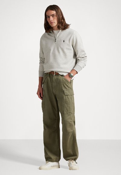 Ljusgrå zip-up sweatshirt med ribbad krage, ihopparad med olivgröna cargobyxor som har sidofickor och dragsko nertill. Vita sneakers.