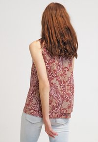 Top senza maniche in un motivo paisley rosso e beige, realizzato in tessuto leggero; presenta un orlo piatto e una texture sottile.