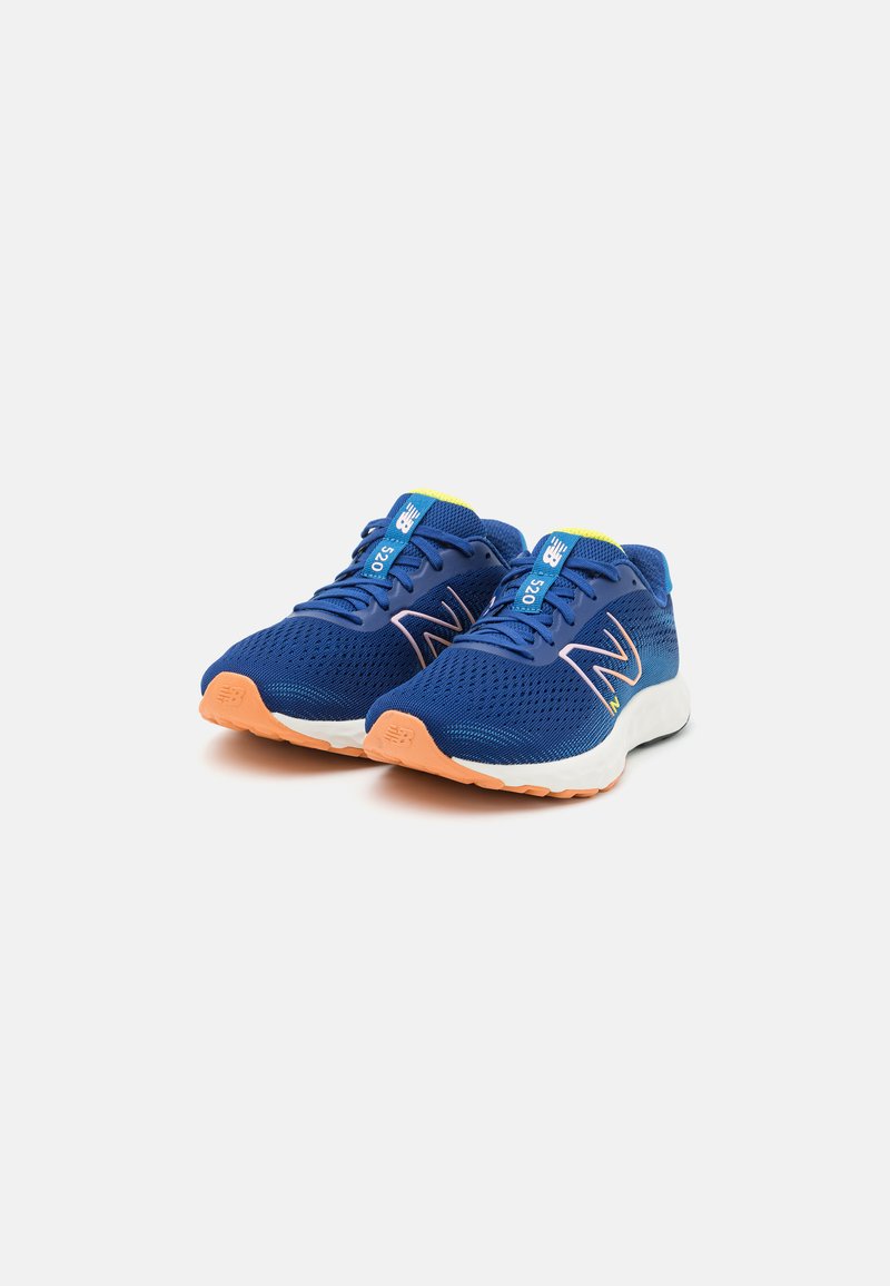 Zapatillas deportivas azules con parte superior de malla y perforaciones, que presentan vivos acentos amarillos, una entresuela blanca y una suela naranja.
