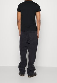 Svart T-shirt med kort ärm som är kombinerad med löst sittande mörkgrå jeans, sedd bakifrån. Enkel design, avslappnad struktur, minimal detaljering.