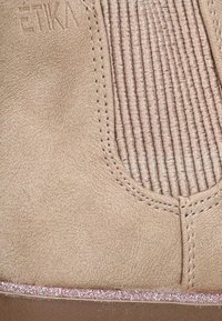 Botín de ante sintético beige con textura acanalada vertical, detalles de costura y un acento brillante en rosa en la base.