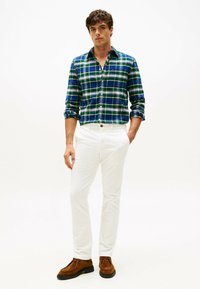 Camisa de franela a cuadros en verde, azul y blanco, combinada con pantalones ajustados blancos y zapatos de ante marrón. Conjunto casual con cuello abotonado.