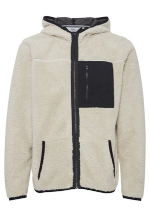 Sudadera de forro polar en crema con detalles en negro. Presenta un bolsillo en el pecho con cremallera, bolsillos frontales y capucha. La textura es suave y esponjosa.
