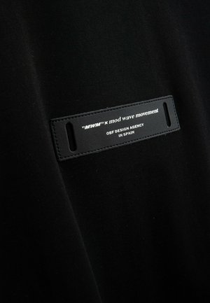 Tela negra con una etiqueta de cuero rectangular con texto en relieve: "mtw" x mod wave movement, OBF DESIGN AGENCY, EN ESPAÑA.