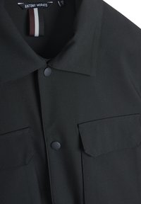 Zwarte button-up shirt met een gestructureerde kraag, twee borstzakken en een gladde stoftextuur. Kenmerkt zich door minimale stiksels en een logotag.