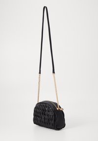 Borsa a spalla nera trapuntata con forma arrotondata, dotata di chiusura con zip e dettagli in catena dorata. Materiale liscio con superficie testurizzata.