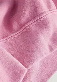 Light pink fleece fabric showing a soft texture, with visible stitching and seams highlighting the garment's construction details.