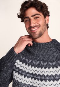 Knit sweater with dark blue and white zigzag pattern, ribbed neckline and cuffs, soft texture, and a relaxed fit.