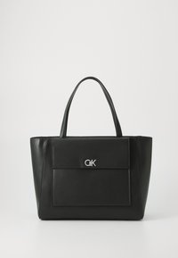 Black leather tote bag with dual handles, featuring a front flap pocket and a silver logo accent; structured shape with smooth texture.