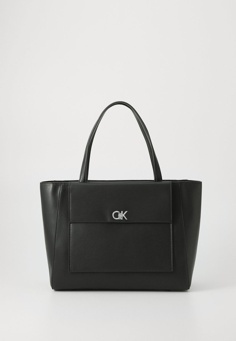 Black leather tote bag with dual handles, featuring a front flap pocket and a silver logo accent; structured shape with smooth texture.