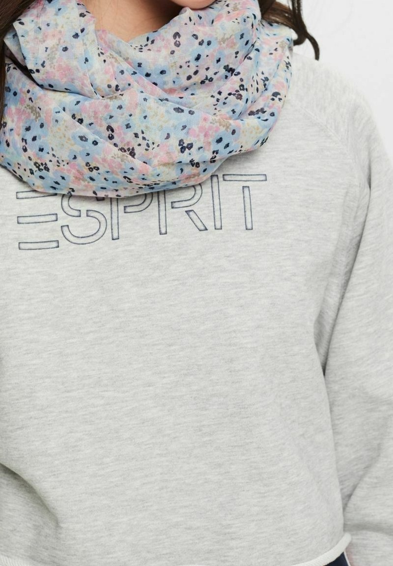 Femme portant un sweat-shirt Esprit gris clair et une écharpe fleurie bleu clair enroulée autour du cou.