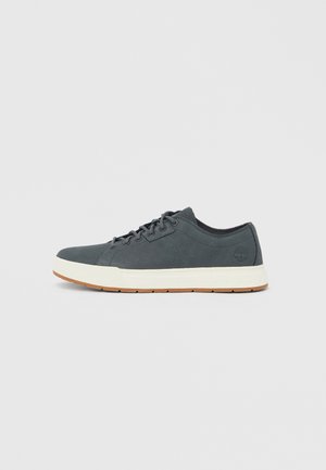 Harmaa lenkkari, jossa on sileä nahkapinta, valkoinen välipohja ja kumipohja. Ominaisuuksiin kuuluu pyöreät nauhat ja logo sivulla.