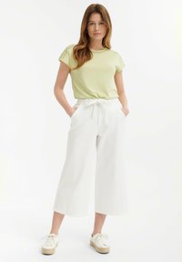 Top verde claro de manga corta con costuras decorativas en los hombros, combinado con pantalones anchos blancos y zapatillas de plataforma beige.