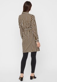 Vestito a camicia a maniche lunghe a righe marroni e bianche con vita cintata, dotato di colletto e polsini a contrasto, abbinato a pantaloni skinny neri.