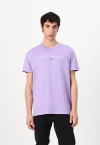 Lavendel T-Shirt mit kurzen Ärmeln aus Baumwolle, ausgestattet mit dem "TOMMY JEANS"-Logo in Weiß auf der Brust und einem runden Ausschnitt.