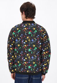 Zwarte, gevoerde jas met een meerkleurig verfspetterpatroon. Ribgebreide manchetten en zoom; lichtgewicht, casual ontwerp, geschikt voor verschillende outfits.
