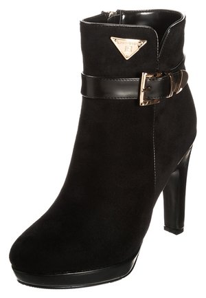 Sort ankelstøvle i ruskind med høj hæl, skinnende sort rem og guldfarvet spænde samt guldfarvet trekantet logoplade på den øvre yderside.