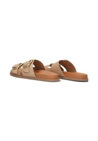Beige slide sandalen met twee decoratieve kleppen en hardware in goudkleur, met een platte bruine rubberen zool en een eenvoudig, gestroomlijnd ontwerp.