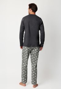 Camiseta gris de manga larga con cuello redondo combinada con pantalones de pijama con un diseño de calaveras. Tejido suave; corte relajado.