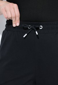Schwarze Jogginghose mit einem strukturierten Bund, der eine Kordel mit weißen Enden und Ösen aufweist. Das Material wirkt weich und flexibel.
