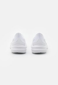 Chaussures de sport blanches avec une tige en mesh texturé, un contrefort de talon rembourré et une semelle en caoutchouc flexible. Design minimaliste sans logo visible.