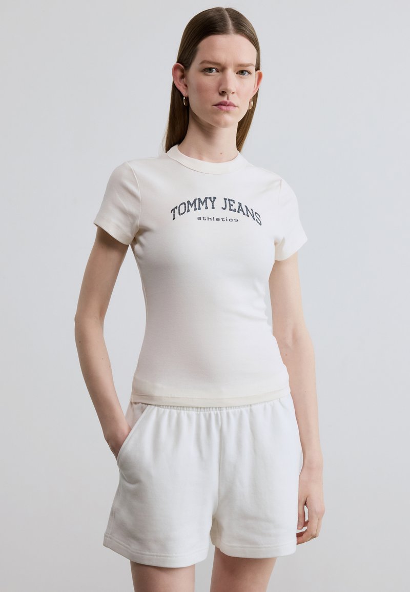 Λευκό βαμβακερό μπλουζάκι με κοντά μανίκια και στρογγυλή λαιμόκοψη, με το κείμενο "TOMMY JEANS athletics" τυπωμένο σε σκούρο μπλε χρώμα στο στήθος. Λευκό σορτς.