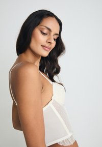 Διαφανές λευκό κορμάκι με δαντελένιες λεπτομέρειες, τιράντες σπαγγέτι και λεπτομέρειες με πουά; μαλακή υφή και βολάν στο στρίφωμα.