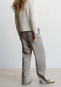 Lässige graue Hosen aus weichem Stoff, kombiniert mit einem cremefarbenen Strickpullover mit strukturiertem Muster und gerippten Bündchen.