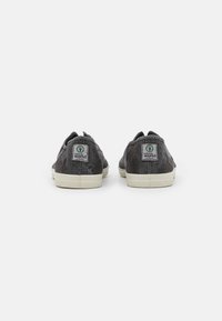 Baskets en toile noires avec semelles en caoutchouc blanches, présentant des logos à l'arrière et une finition texturée, un design à bout rond et un dos sans lacets.