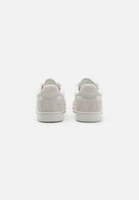 Ein Paar Low-Top-Sneaker mit einem obermaterial aus hellbeigem Leder und Wildlederakzenten, einer runden Ferse und einer Gummisohle. Zwei hintere Zuglaschen sind sichtbar.