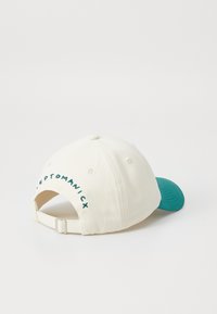 Casquette en coton blanc avec une visière teal, ornée d'un texte brodé vert à l'arrière et d'une sangle ajustable à l'arrière.
