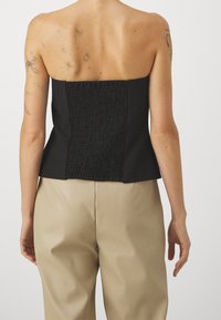 Top nero senza spalline con un design posteriore a trama e arricciato; parte anteriore liscia; abbinato a pantaloni beige.