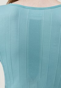 Jasnoniebieska koszula z fakturowanym wzorem i pionowymi paskami oraz centralnym panelem z siatki na plecach. Zawiera małą metkę z logo.